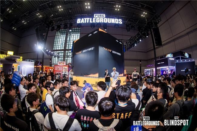 职业选手GODV在舞台上展示白色联名外套,台下观众举手机拍摄