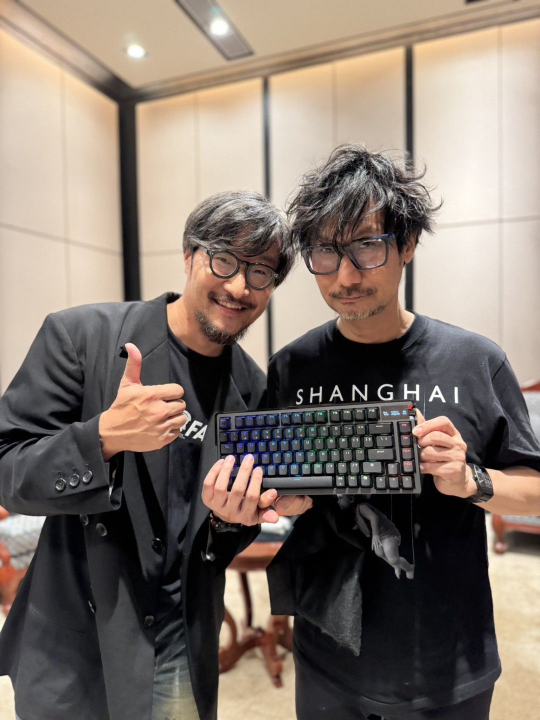 小岛秀夫手持ROG机械键盘微笑展示，键盘特写可见‘HIDEO’激光雕刻字样，背景为BW2025展台灯光