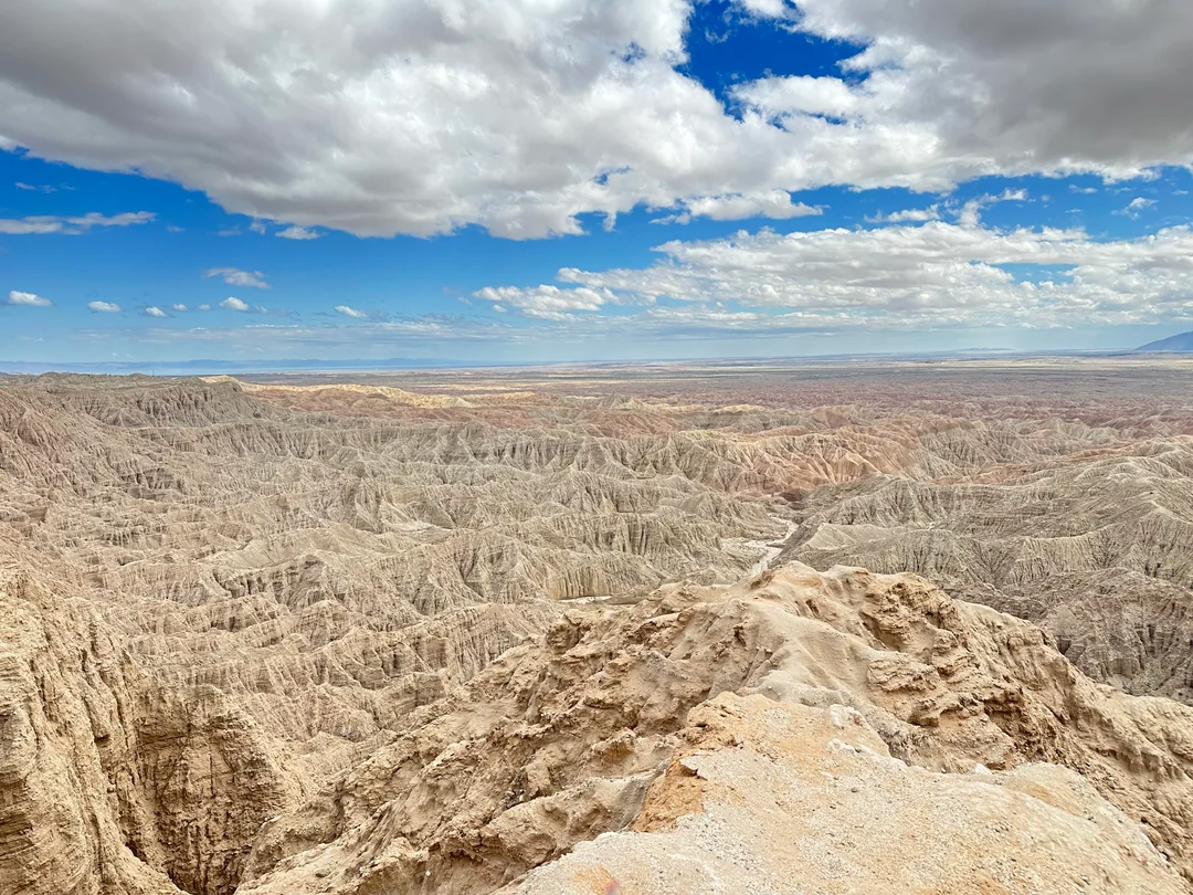 Anza-Borrego沙漠日落场景:低角度阳光将长条形砂岩投下锐利阴影,地面泛起金属质感的暖金色反光,远处地平线处有微弱大气辉光